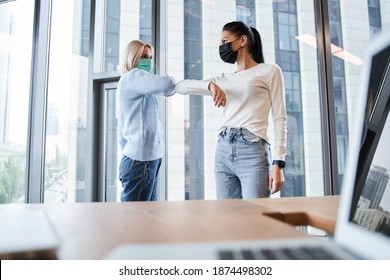 Smiling Diverse Female Colleagues Wearing Protective Face Masks Greeting Bumping Elbows At Workplace. Woman Coworkers In Facial Covers Protect From COVID-19 Coronavirus In Office, Healthcare Concept