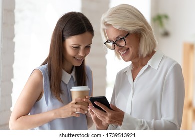 Smiling diverse female employees enjoy coffee break browse wireless Internet on smartphone together, happy woman colleagues coworkers have fun chatting and talking using modern cellphone in office - Powered by Shutterstock