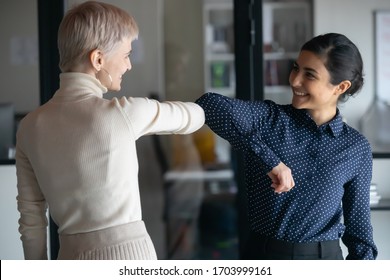 Smiling Diverse Female Employees Greeting Bumping Elbows At Workplace, Happy Woman Colleagues Say Hello In Office, Protect From Coronavirus COVID-19 Pandemic, Corona, Healthcare Concept