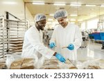 Smiling diverse food factory workers collecting freshly baked biscuits at food processing industry.