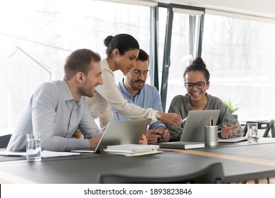 Smiling diverse young colleagues gather at desk in office look at laptop screen brainstorming at meeting together, happy multiracial employees cooperate using computer at briefing, teamwork concept - Shutterstock ID 1893823846