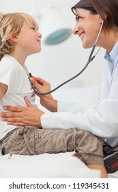 Smiling Doctor Auscultating A Child With A Stethoscope In Examination Room