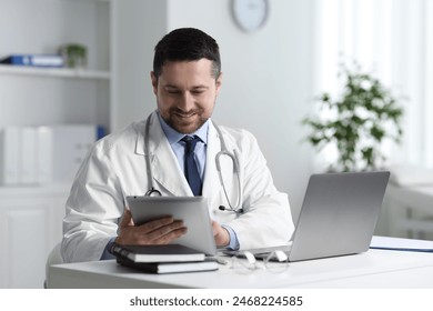 Smiling doctor having online consultation via tablet at table in clinic - Powered by Shutterstock