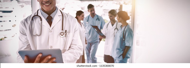 Médico sorridente segurando tablet digital na frente de sua equipe médica