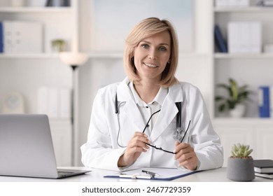 Smiling doctor with laptop having online consultation at table in office - Powered by Shutterstock