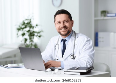 Smiling doctor with laptop at table in clinic. Online consultation - Powered by Shutterstock