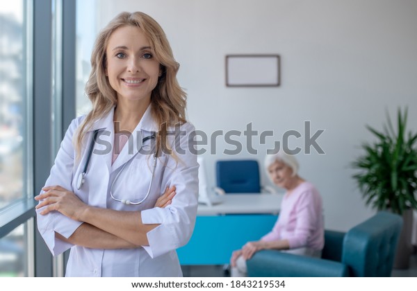 Smiling doctor. Long-haired blonde doctor\
standing with arms crossed and\
smiling