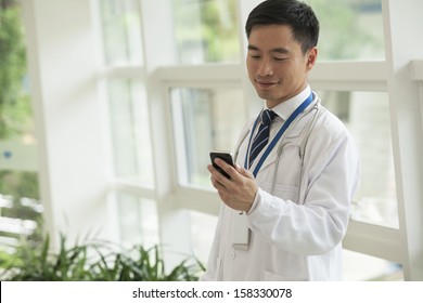 Smiling Doctor Looking Down At His Phone In Hospital Lobby