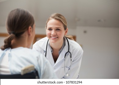 Smiling Doctor Looking At A Patient On A Wheelchair In Hospital Hallway