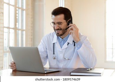 Smiling doctor using headset with microphone working on laptop, looking at screen, consulting patient online, sitting at desk, therapist wearing white uniform making video call, telemedicine - Powered by Shutterstock