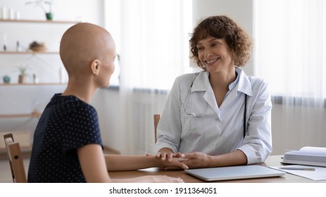 Smiling doctor in white medical uniform comfort support hairless female cancer patient at meeting in hospital. Caring female nurse or GP hold hand show support bald woman struggle with oncology.