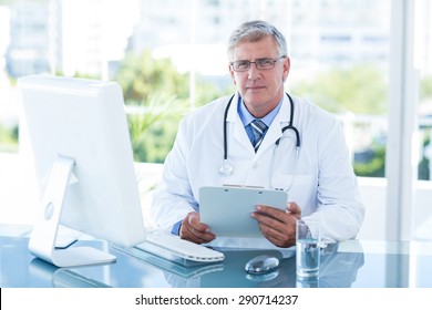 Smiling Doctor Working On Computer At His Desk In Medical Office