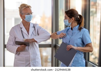 Smiling doctors wearing protective face masks greeting bumping elbows at workplace. COVID-19 