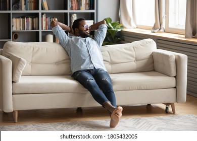 Smiling Dreamy African American Man Sitting On Cozy Couch With Hands Behind Head, Thinking About Good Future, Looking To Aside, Dreaming About New Opportunities, Enjoying Lazy Weekend At Home