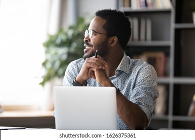 Smiling dreamy african business man student professional wear glasses look away dream about good future vision relax thinking of new creative ideas working studying on laptop sit at home office desk