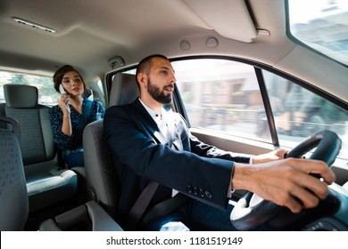 Smiling driver dirving a car with elegant businesswoman. Woman talking on mobie phone.
