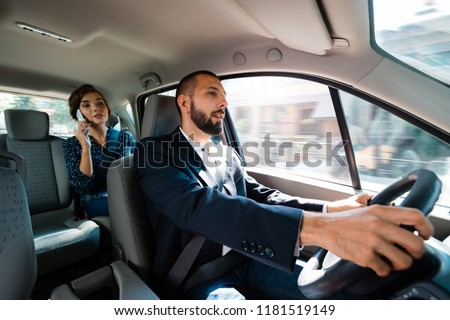 Smiling driver dirving a car with elegant businesswoman. Woman talking on mobie phone.