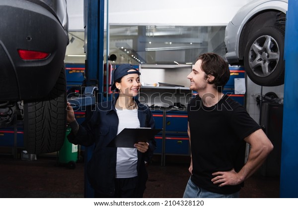 Smiling driver looking at mechanic with clipboard\
near car in service
