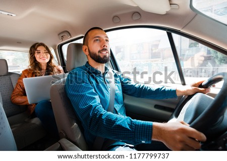 Smiling driver talking with female passenger. Woman using laptop in the background.