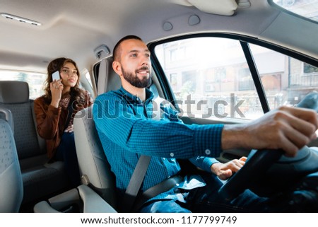 Smiling driver talking with female passenger. Woman using mobile phone in the background.