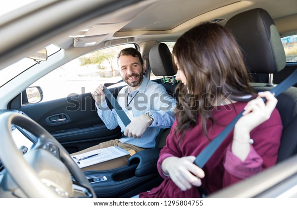 Smiling driving instructor teaching woman to fasten\
seatbelt of car