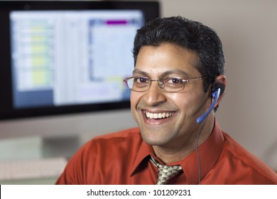 Smiling East Indian customer service rep with headset and computer monitor