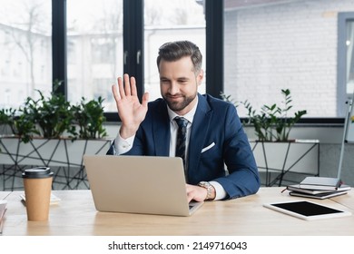 smiling economist waving hand during video call on laptop in office - Powered by Shutterstock