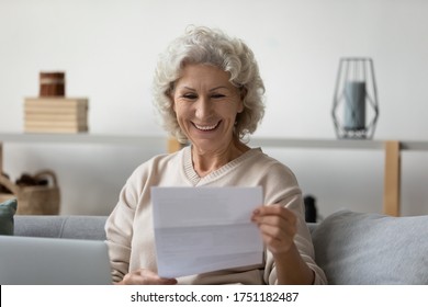 Smiling elderly 60s woman sit on couch in living room feel overjoyed reading good news in postal paper letter, happy senior 50s female get pleasant paperwork bank notice or post correspondence