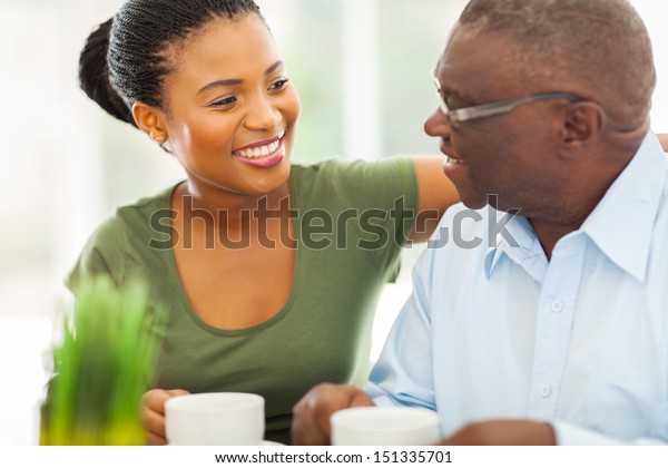 smiling elderly african american man enjoying\
coffee with his granddaughter at\
home