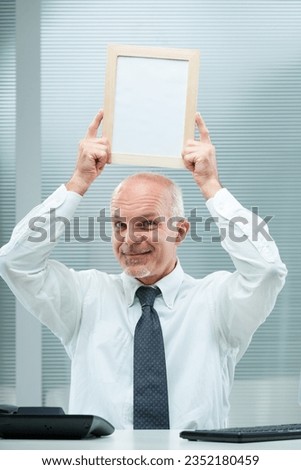 Smiling elderly businessman raises an empty board perfect for copyspace. In the milieu, a mature figure in a white shirt and tie