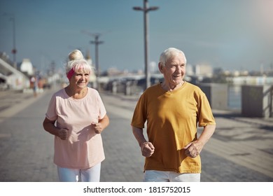 Smiling Elderly Caucasian Woman And A Pleased Gray-haired Man In Casual Wear Power Walking Outdoors