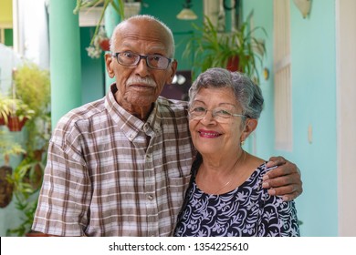 An smiling elderly couple, both wearing glasses.