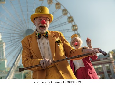 Smiling Elderly Couple In Ridiculous Artistic Clothes Relaxing Near Ferris Wheel