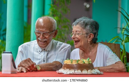 Smiling Elderly Couple Sitting At A Table Looking At A Cell Phone