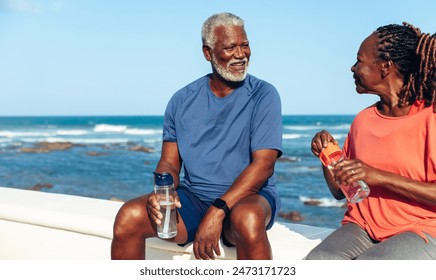 Smiling elderly couple taking a break by the seaside, holding water bottles and enjoying the moment. Perfect for concepts of mature relationships, health, and relaxation. - Powered by Shutterstock