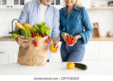 Smiling elderly couple unpacking bag of fresh, colorful vegetables and bread in their bright modern kitchen, happy senior spouses return to home after food shopping, checking groceries, cropped shot - Powered by Shutterstock