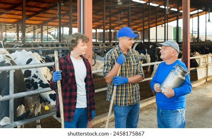 Smiling elderly farmer friendly chatting with son and grandson during break from work at family dairy farm, standing near outdoor stall with cows - Powered by Shutterstock