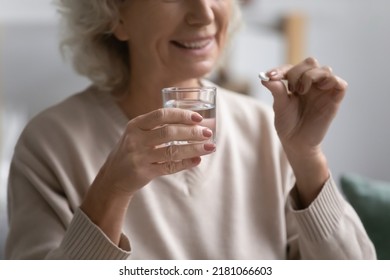 Smiling elderly female patient holding pill and glass of water. Senior mature woman taking daily dose of prescribed meds against depression, mental disorders, flu, insomnia, pain. Elderly treatment - Powered by Shutterstock