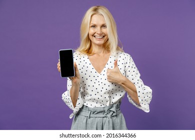 Smiling Elderly Gray-haired Blonde Woman Lady 40s 50s Years Old In White Dotted Blouse Hold Mobile Cell Phone With Blank Empty Screen Showing Thumb Up Isolated On Violet Background Studio Portrait