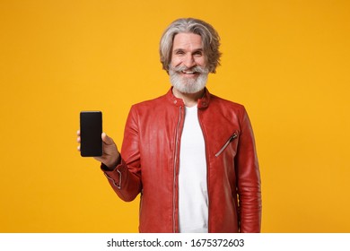 Smiling elderly gray-haired mustache bearded man in red leather jacket isolated on yellow orange background. People lifestyle concept. Mock up copy space. Hold mobile phone with blank empty screen - Shutterstock ID 1675372603