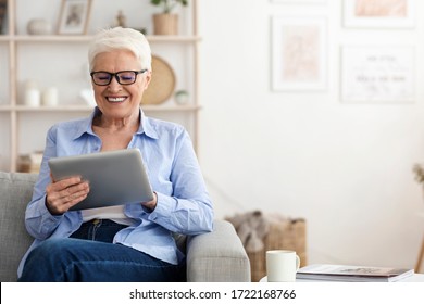 Smiling elderly lady wearing glasses using digital tablet at home, browsing internet or watching videos, copy space - Powered by Shutterstock