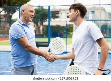 Smiling elderly man paddle tennis player shaking hands with his young opponent after match on outdoor court, thanking for fair and interesting game. Mutual respect concept of competitors.. - Powered by Shutterstock