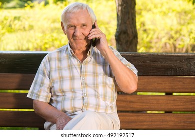 Smiling elderly man with phone. Senior male on a bench. I miss my relatives. Grandpa calls home. - Powered by Shutterstock