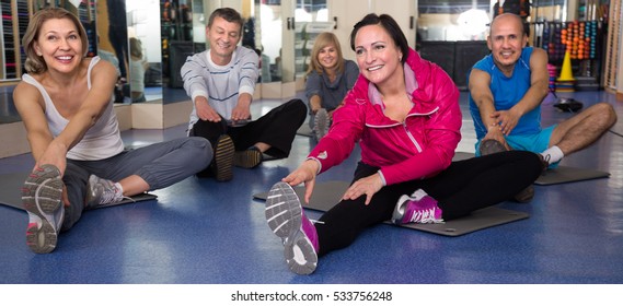 Smiling Elderly People Doing Exercise On Mat In Modern Gym