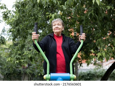 Smiling elderly woman is doing exercises on simulator outdoors in the yard.  Active life of pensioners. Adaptation of pensioners in the modern world. Prevention of Alzheimer's disease, sclerosis etc - Shutterstock ID 2176563601