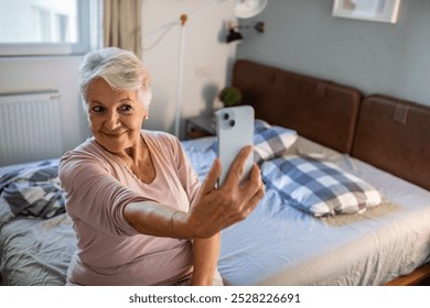 Smiling elderly woman using smartphone while sitting on bed - Powered by Shutterstock