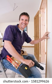 Smiling Electrician Holding Drill Working On Wall Outlet At Camera