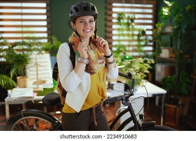 smiling elegant 40 years old business woman in bike helmet with bicycle in modern eco office. - Powered by Shutterstock