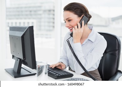 Smiling elegant businesswoman using landline phone and computer in a bright office - Powered by Shutterstock