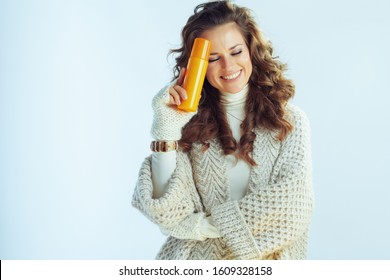 Smiling Elegant Middle Age Woman With Long Wavy Hair In Neck Sweater And Cardigan With Suntan Lotion Isolated On Winter Light Blue Background.